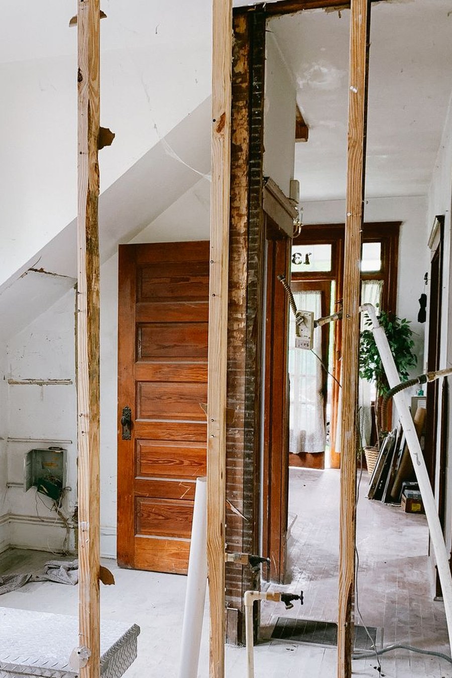 A room stripped back to its studwork, with the original panelled door and brickwork exposed